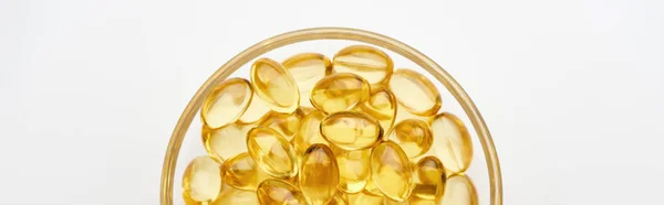 Top view of golden fish oil capsules in glass bowl on white background, panoramic shot — Stock Photo