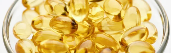 Close up view of golden fish oil capsules in glass bowl on white background, panoramic shot — Stock Photo