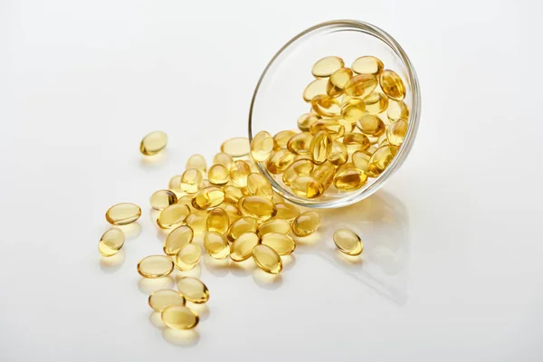 Capsule di olio di pesce dorato in ciotola di vetro su sfondo bianco — Foto stock