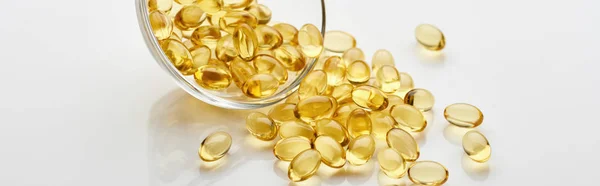 Golden fish oil capsules in glass bowl on white background, panoramic shot — Stock Photo