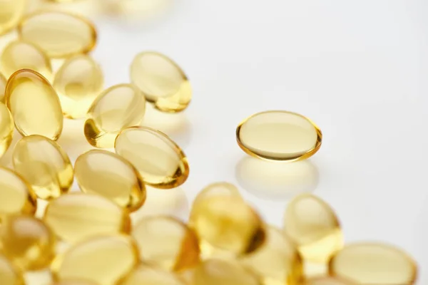 Close up view of golden fish oil capsules scattered on white background — Stock Photo