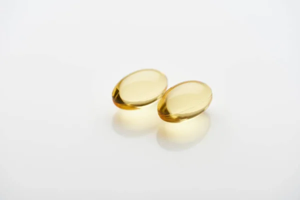 Two golden fish oil capsules on white background — Stock Photo