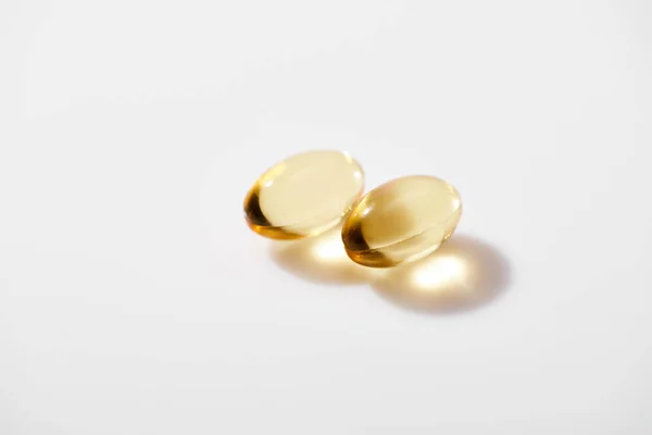 Two golden fish oil capsules on white background — Stock Photo