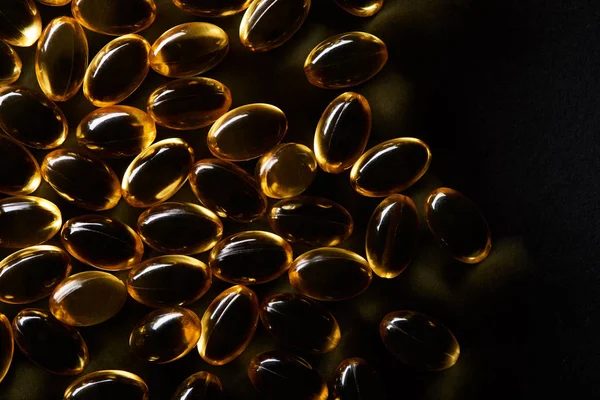 Vue de dessus des capsules d'huile de poisson dorées sur fond noir dans l'obscurité — Photo de stock