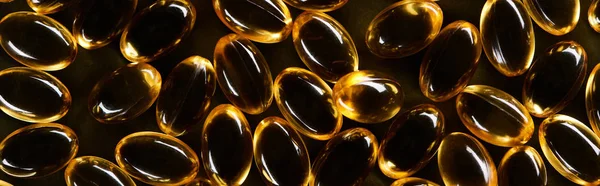 Top view of golden fish oil capsules on black background in dark, panoramic shot — Stock Photo