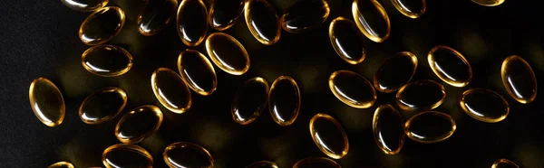 Top view of golden fish oil capsules on black background in dark, panoramic shot — Stock Photo