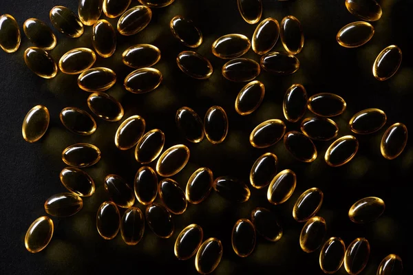 Vista superior de cápsulas de aceite de pescado dorado sobre fondo negro en oscuridad - foto de stock