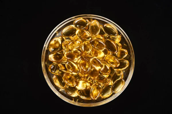 Top view of golden fish oil capsules in glass bowl isolated on black — Stock Photo