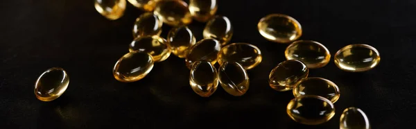 Golden fish oil capsules scattered isolated on black, panoramic shot — Stock Photo