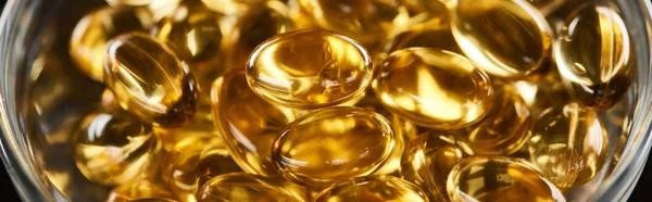 Close up view of golden fish oil capsules in glass bowl, panoramic shot — Stock Photo