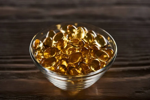 Golden fish oil capsules scattered on wooden table — Stock Photo