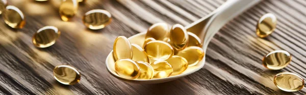 Golden fish oil capsules in spoon on wooden table, panoramic shot — Stock Photo