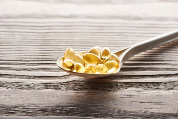 Golden fish oil capsules in spoon on wooden table — Stock Photo