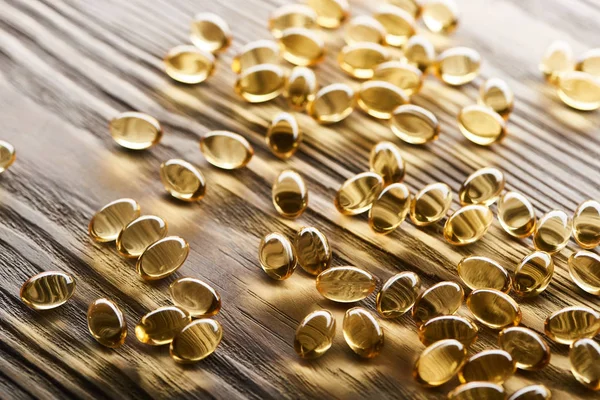 Capsules d'huile de poisson dorée dispersées sur une table en bois — Photo de stock