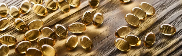 Golden fish oil capsules scattered on wooden table, panoramic shot — Stock Photo