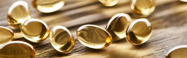 Close up view of golden fish oil capsules scattered on wooden table, panoramic shot — Stock Photo