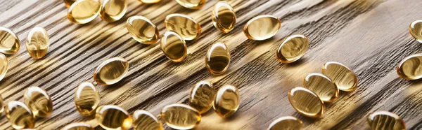 Capsules d'huile de poisson dorées éparpillées sur une table en bois, vue panoramique — Photo de stock