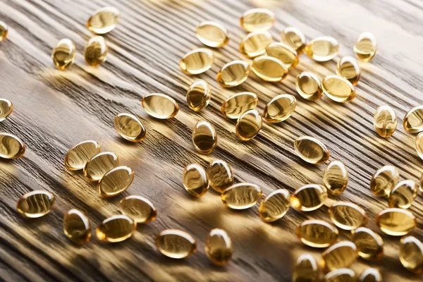 Cápsulas de óleo de peixe dourado espalhadas na mesa de madeira — Fotografia de Stock