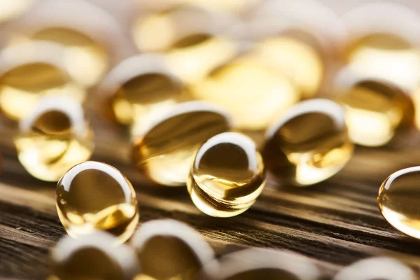 Close up view of golden fish oil capsules scattered on wooden table — Stock Photo