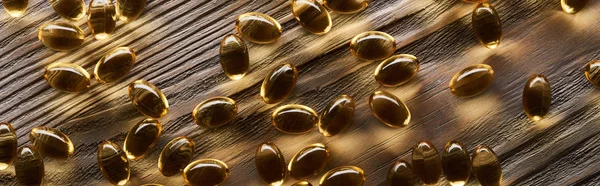 Close up view of shiny golden fish oil capsules scattered on wooden table, panoramic shot — Stock Photo