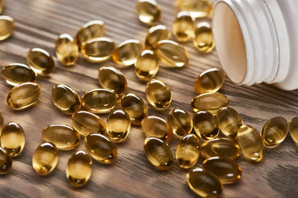 Golden fish oil capsules scattered from plastic container on wooden table — Stock Photo