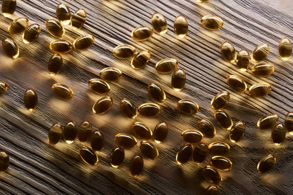 Brilhantes cápsulas de óleo de peixe dourado espalhadas na mesa de madeira — Fotografia de Stock