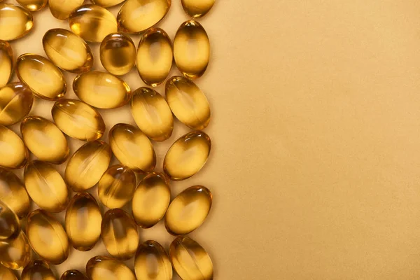 Vue de dessus des capsules d'huile de poisson brillantes dorées sur fond jaune avec espace de copie — Photo de stock