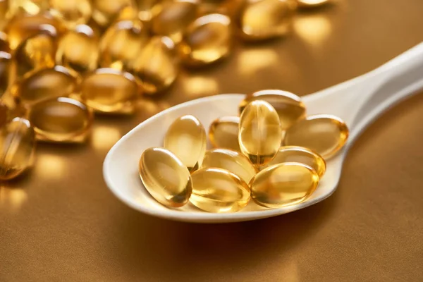 Close up view of shiny fish oil capsules in spoon on golden background — Stock Photo