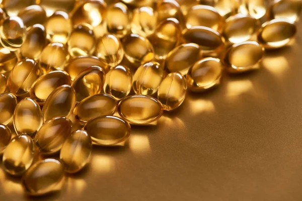 Close up view of shiny fish oil capsules on golden background with copy space — Stock Photo