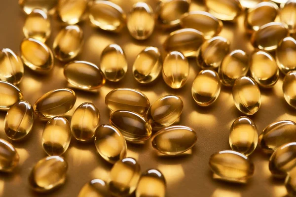 Shiny fish oil capsules on golden background — Stock Photo