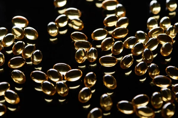 Cápsulas de aceite de pescado dorado brillante dispersas sobre fondo negro - foto de stock