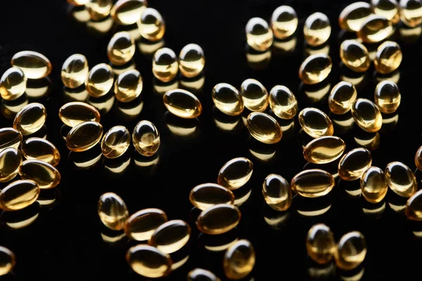 Brilhante cápsulas de óleo de peixe dourado espalhadas no fundo preto — Fotografia de Stock