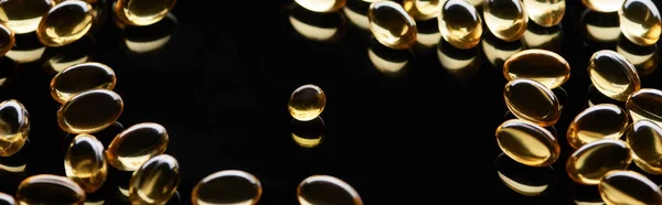 Goldglänzende Fischöl-Kapseln auf schwarzem Hintergrund verstreut, Panoramaaufnahme — Stockfoto