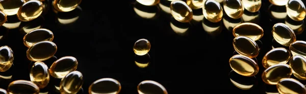 Shiny golden fish oil capsules scattered on black background, panoramic shot — Stock Photo