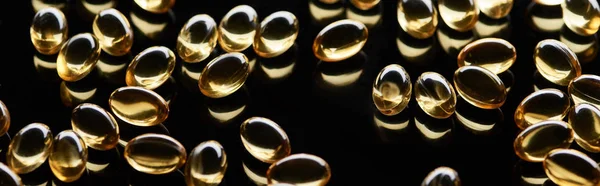 Shiny golden fish oil capsules scattered on black background, panoramic shot — Stock Photo