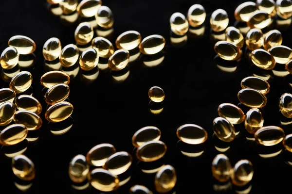 Brilhante cápsulas de óleo de peixe dourado espalhadas no fundo preto — Fotografia de Stock