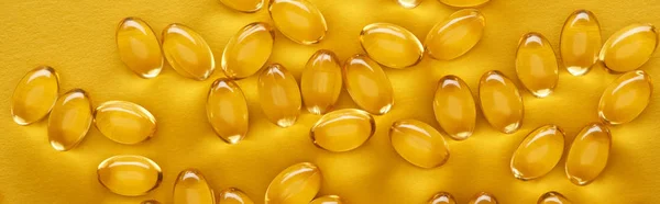 Vista superior de cápsulas de aceite de pescado brillante dorado dispersas sobre fondo amarillo brillante, plano panorámico - foto de stock