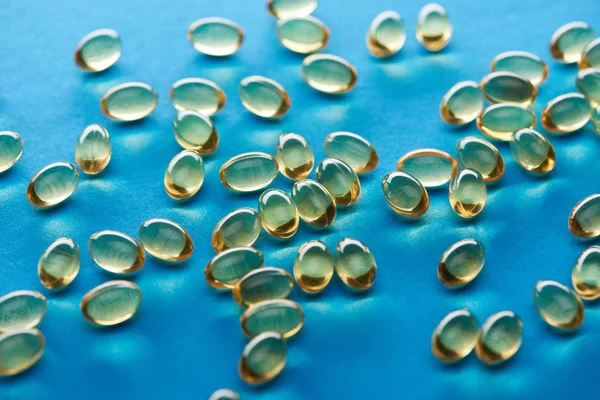 Cápsulas de óleo de peixe dourado espalhadas no fundo azul — Fotografia de Stock
