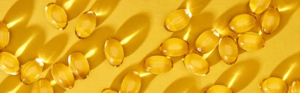 Vista superior de cápsulas de aceite de pescado brillante dorado dispersas sobre fondo amarillo brillante, plano panorámico - foto de stock
