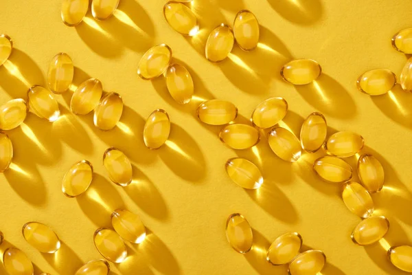Vista dall'alto d'oro lucido capsule di olio di pesce sparsi su sfondo giallo brillante — Foto stock