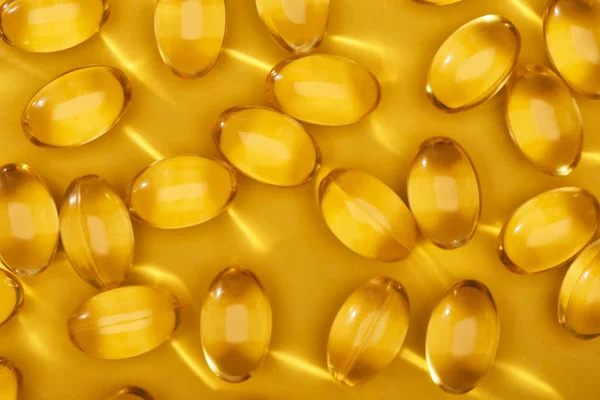 Vista superior de cápsulas de aceite de pescado dorado brillante dispersas sobre fondo amarillo brillante - foto de stock