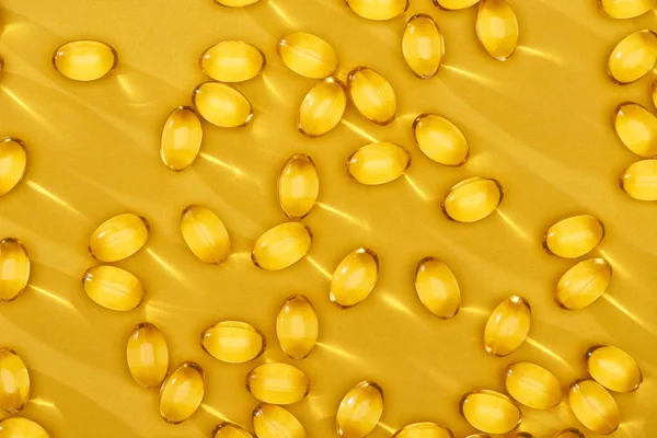 Vista superior de ouro brilhante cápsulas de óleo de peixe espalhadas no fundo amarelo brilhante — Fotografia de Stock