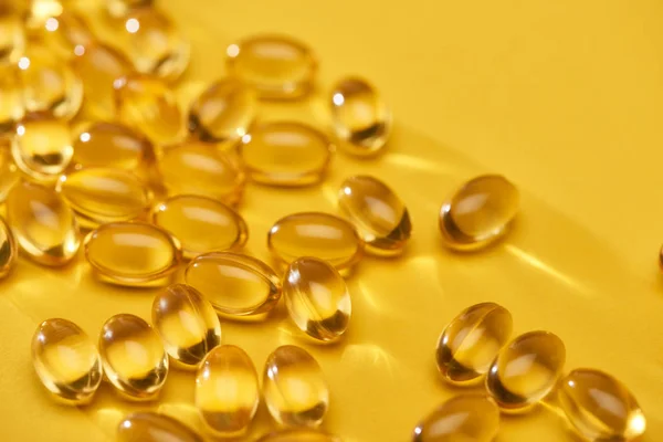 Vue rapprochée de capsules d'huile de poisson brillantes dorées éparpillées sur fond lumineux jaune — Photo de stock