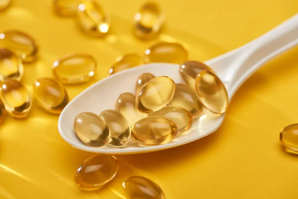 Close up view of golden shiny fish oil capsules scattered from spoon on yellow bright background — Stock Photo