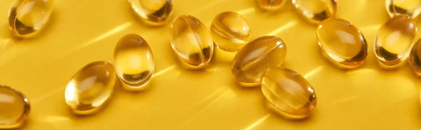Vista de cerca de cápsulas de aceite de pescado brillante dorado dispersas sobre fondo amarillo brillante, plano panorámico - foto de stock