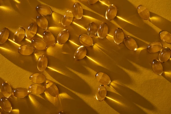 Capsules d'huile de poisson brillantes dorées dispersées sur fond jaune dans l'obscurité — Photo de stock