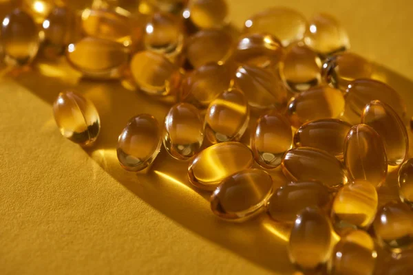 Vue rapprochée des capsules d'huile de poisson brillantes dorées éparpillées sur fond jaune dans l'obscurité — Photo de stock