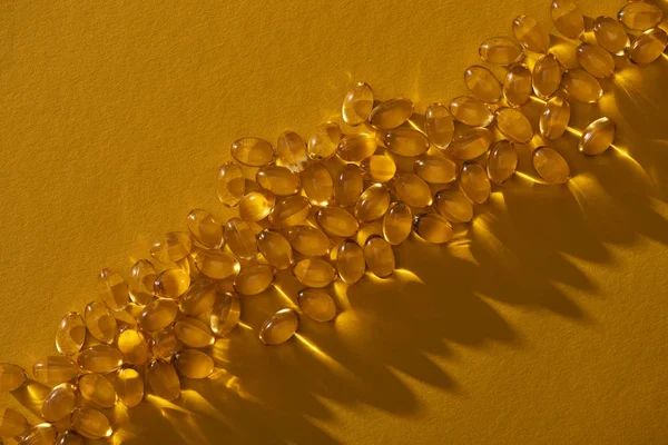 Вид зверху на золоті блискучі рибні масляні капсули на жовтому тлі в темряві — стокове фото