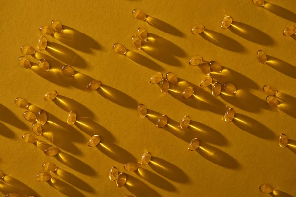 Vue de dessus des capsules d'huile de poisson brillantes dorées éparpillées sur fond jaune dans l'obscurité — Photo de stock