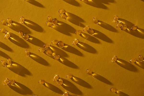 Vue de dessus des capsules d'huile de poisson brillantes dorées éparpillées sur fond jaune dans l'obscurité — Photo de stock